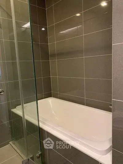 Modern bathroom with sleek gray tiles and a glass-enclosed bathtub.