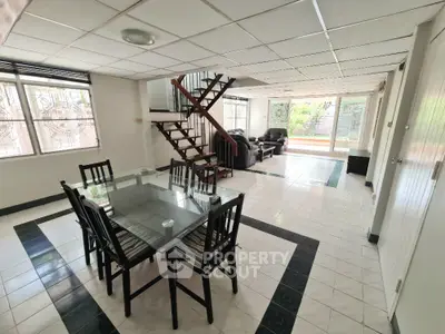 Spacious open-plan living and dining area with modern glass table and stylish staircase.