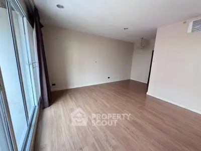 Spacious empty living room with wooden flooring and large windows for natural light.