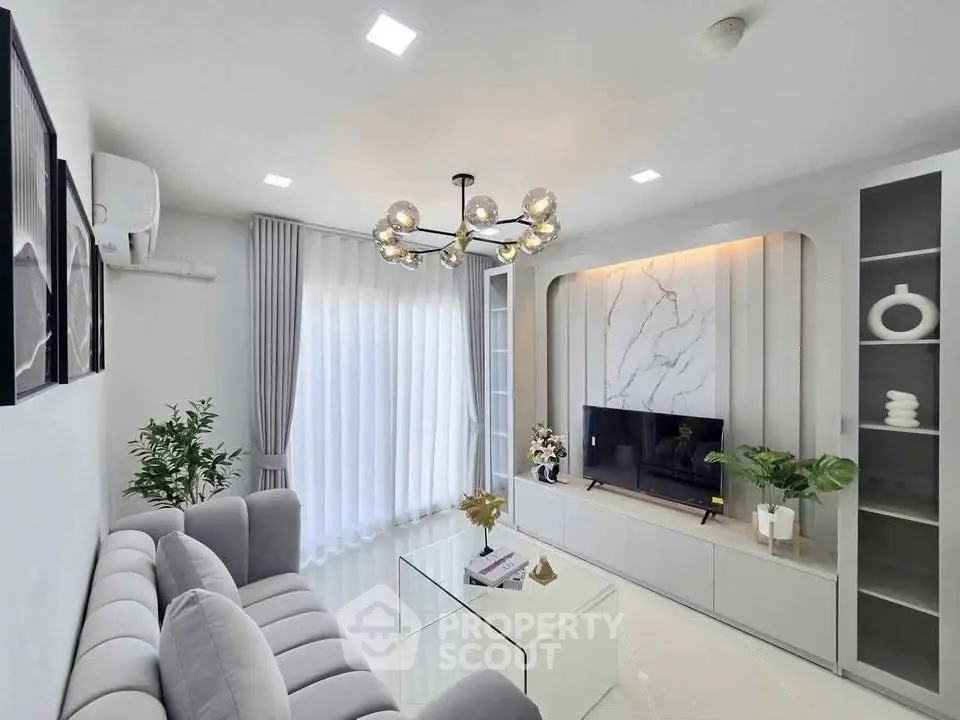Modern living room with elegant decor, featuring a stylish chandelier, sleek TV unit, and plush gray sofa.