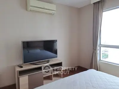 Cozy bedroom with TV and air conditioning, featuring large window for natural light.