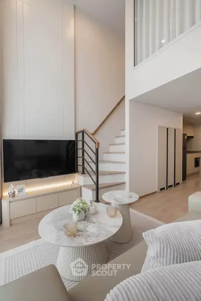 Modern living room with high ceiling and stylish decor, featuring a sleek staircase and elegant furniture.