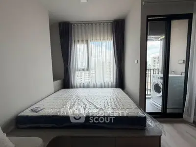 Modern bedroom with balcony and city view, featuring a new mattress and washing machine.