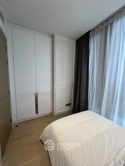 Modern bedroom with sleek wardrobe and large window with curtains.