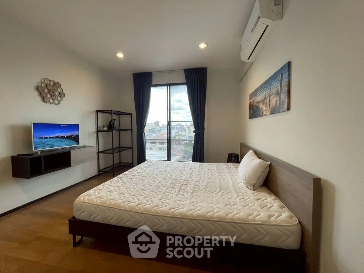 Modern bedroom with large window and city view, featuring a comfortable bed and stylish decor.
