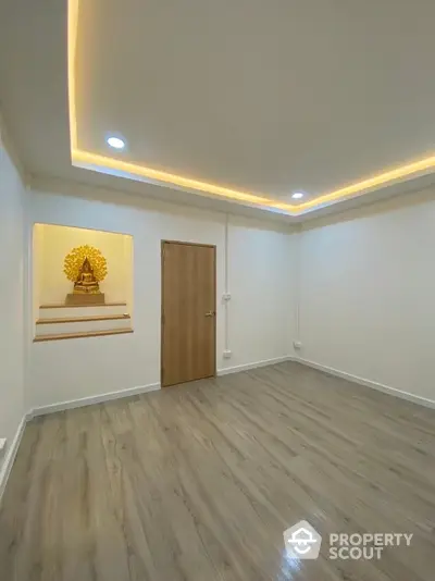 Spacious room with wooden flooring and recessed lighting, featuring a decorative niche with a statue.