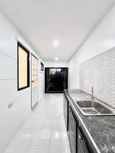 Modern kitchen with sleek countertops and stylish backsplash in a bright, narrow layout.