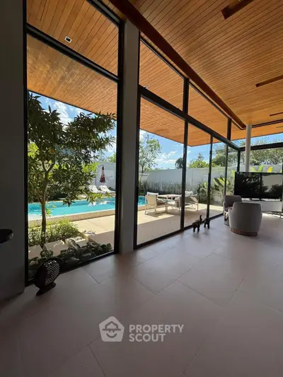 Luxurious living room with floor-to-ceiling windows overlooking a serene pool and lush garden.