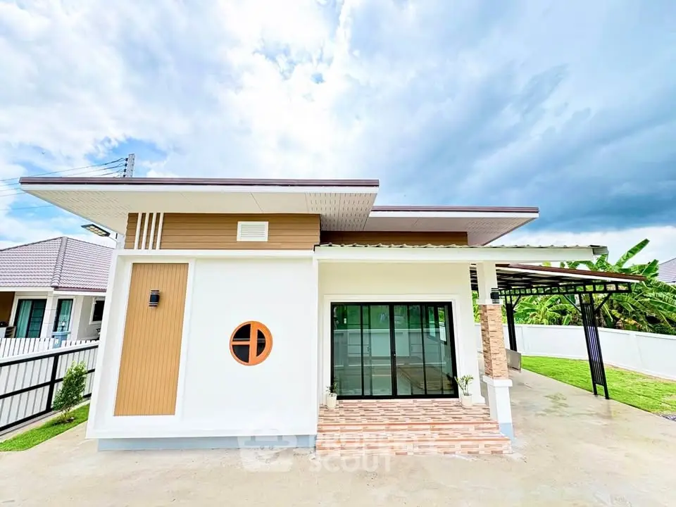 Modern single-story house with unique circular window and spacious driveway, surrounded by lush greenery.