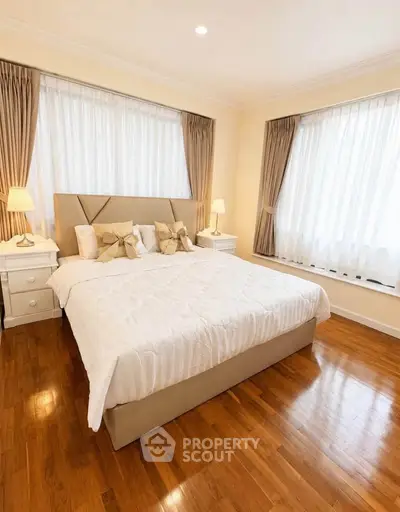 Elegant bedroom with hardwood floors and large windows, featuring a cozy bed and stylish decor.
