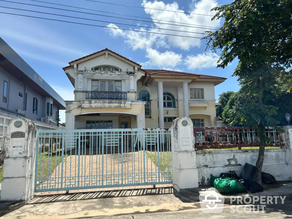 Charming two-story house with gated entrance and spacious front yard under a clear blue sky.