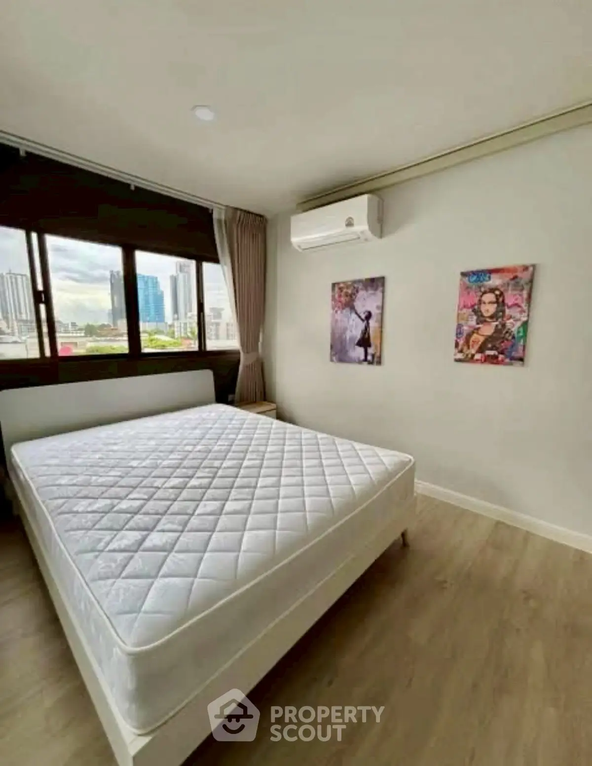 Modern bedroom with large window and city view, featuring stylish wall art and air conditioning.