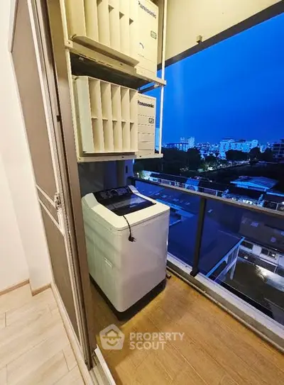 Compact balcony with washing machine and city view at dusk