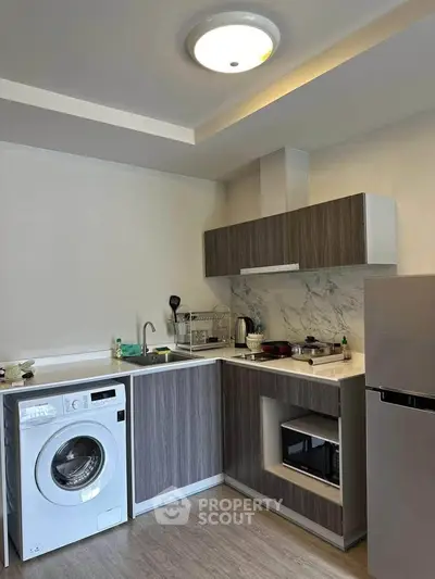 Modern kitchen with washing machine, sleek cabinetry, and built-in appliances in a compact layout.