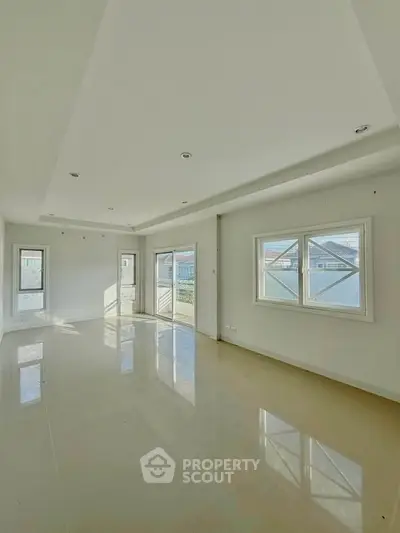 Spacious sunlit living room with large windows and glossy floors in modern home.