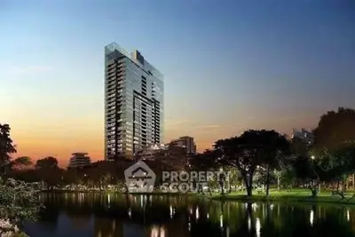 Stunning high-rise building with serene park and water view at sunset, perfect for luxury living.