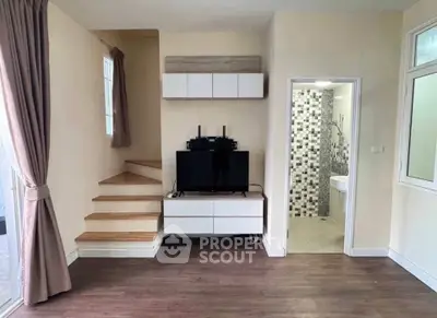 Modern living room with TV, staircase, and bathroom entrance, featuring stylish decor and natural light.
