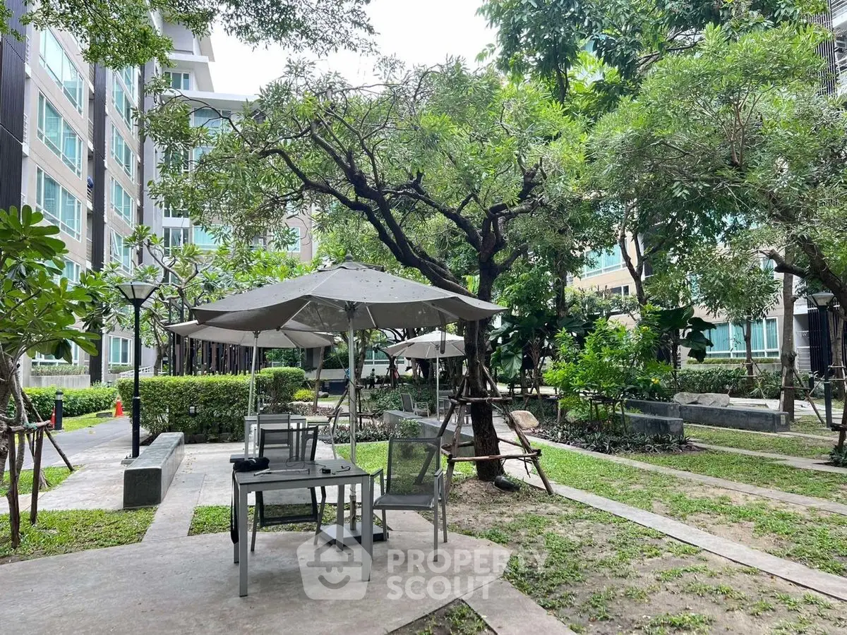 Charming garden area in modern residential complex with outdoor seating and lush greenery.