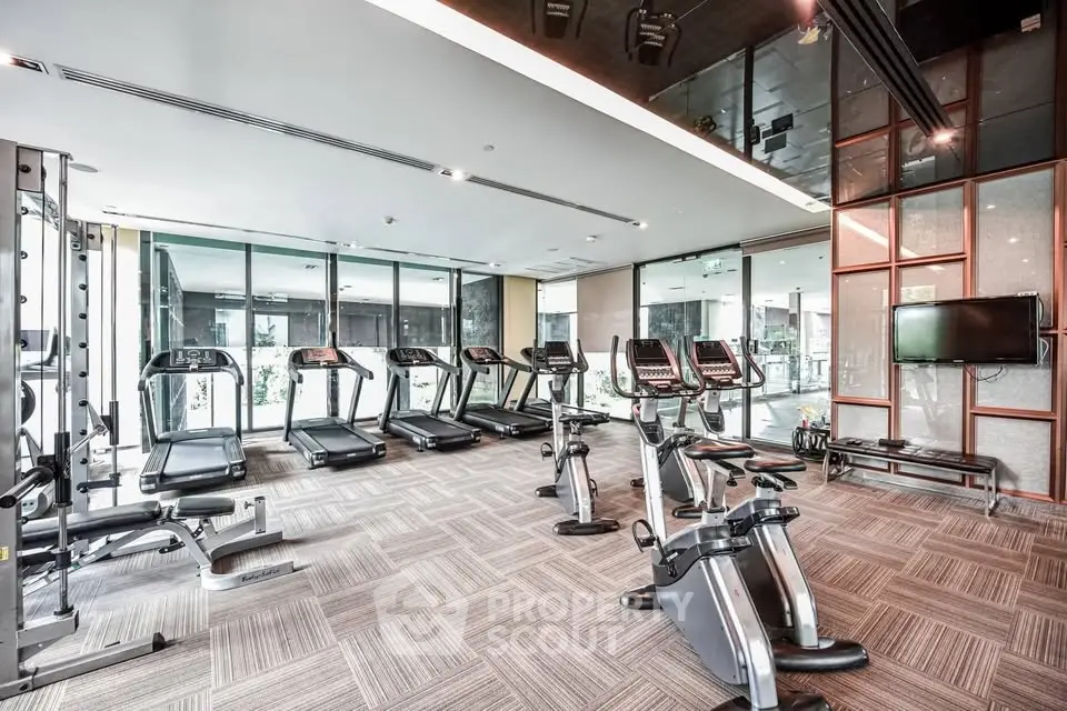 Modern gym with state-of-the-art equipment and floor-to-ceiling windows in luxury residential building.