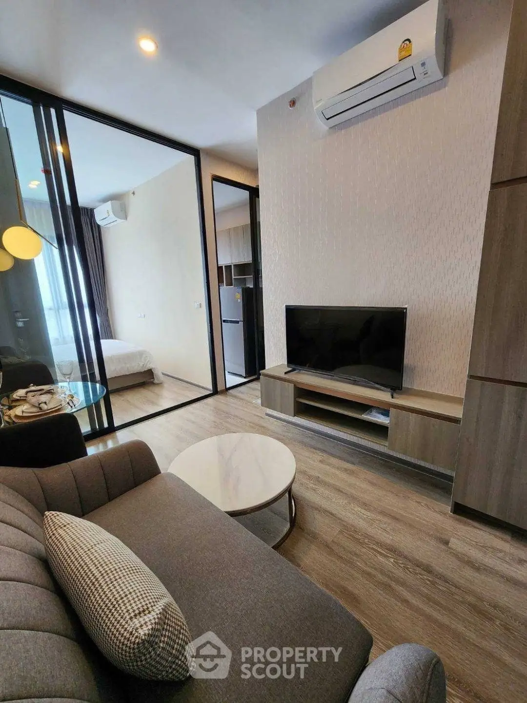 Modern living room with sleek design, featuring a cozy sofa, flat-screen TV, and air conditioning, leading to a bedroom.