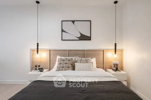 Modern bedroom with stylish decor and pendant lighting, featuring a cozy bed and contemporary artwork.