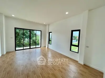 Spacious room with large windows and wooden flooring, offering natural light and garden view.