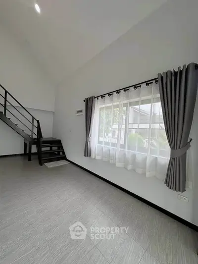 Spacious modern living room with large window and staircase, perfect for natural light lovers.