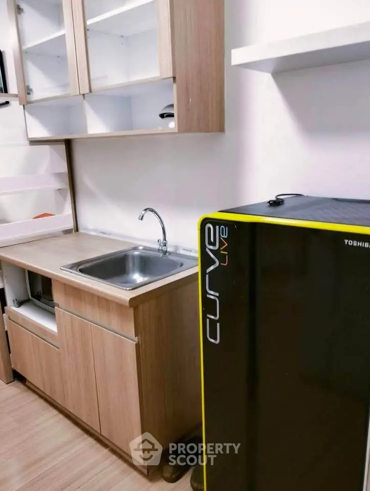 Compact kitchen with wooden cabinets and sleek black fridge in modern apartment.