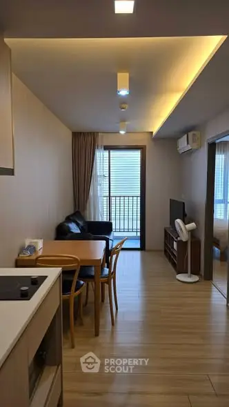 Modern living room with open layout and balcony access, featuring sleek furniture and wooden flooring.