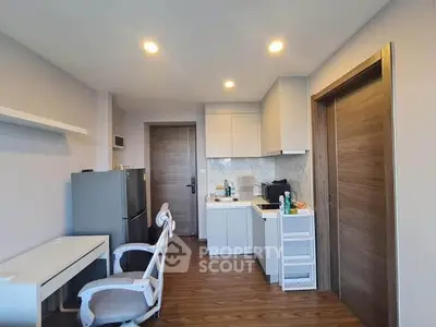 Modern compact kitchen with sleek design and wooden flooring, featuring a desk and chair for versatile use.