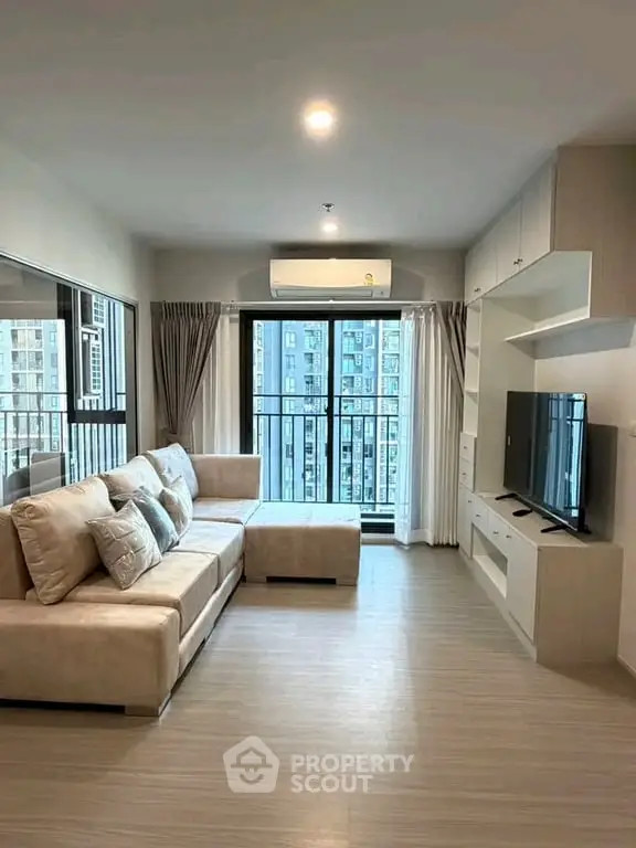 Modern living room with large windows and city view, featuring a cozy sectional sofa and sleek entertainment unit.