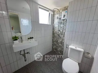 Modern bathroom with stylish tiles and natural light, featuring a sleek sink and shower area.