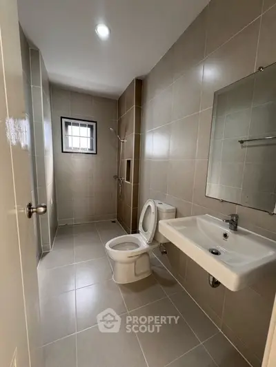 Modern bathroom with sleek fixtures and neutral tiles, featuring a shower and large mirror.