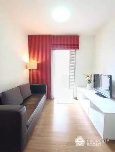 Cozy living room with modern sofa and TV unit, featuring bright natural light and stylish red curtains.