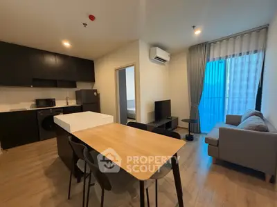 Modern open-layout living room with kitchen, featuring sleek furniture and natural light from large windows.