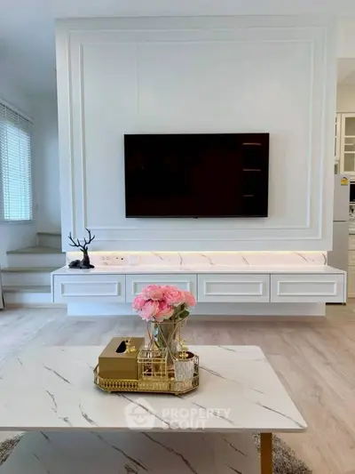 Elegant living room with modern decor, featuring a wall-mounted TV and stylish coffee table with floral centerpiece.