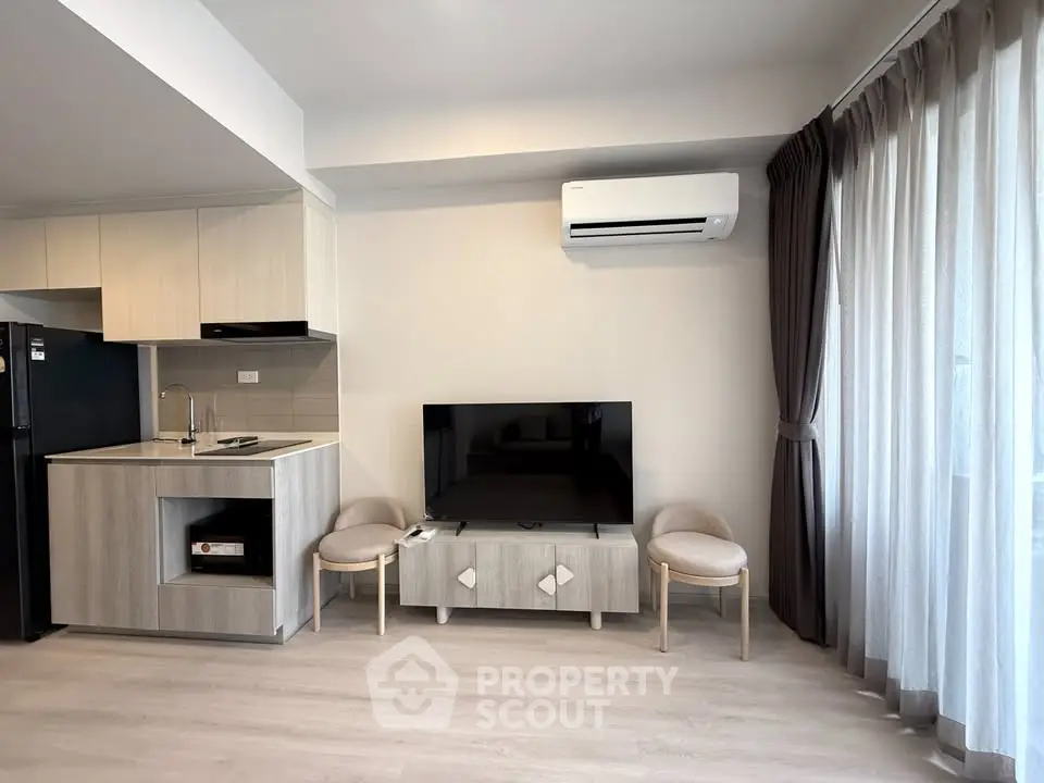 Modern living room with sleek kitchen, air conditioning, and natural light from large windows.