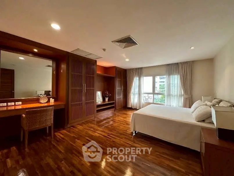 Spacious bedroom with wooden flooring and large windows offering natural light.