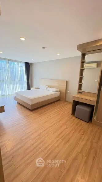 Spacious bedroom with modern wooden flooring and large windows for natural light.