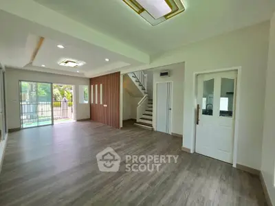 Spacious modern living room with wooden flooring and large windows overlooking greenery.
