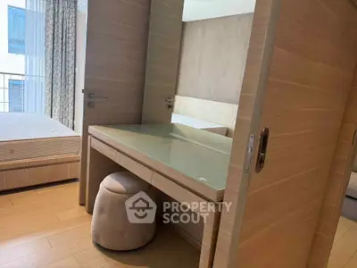 Modern bedroom with stylish wooden furniture and glass-top desk, featuring a cozy ambiance and natural light.