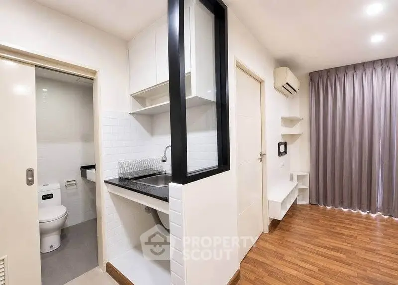 Modern apartment interior with compact kitchen and bathroom, featuring sleek design and wooden flooring.