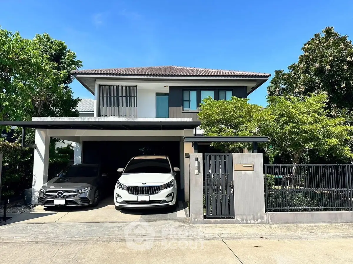 Modern two-story house with two cars parked in driveway, surrounded by lush greenery.