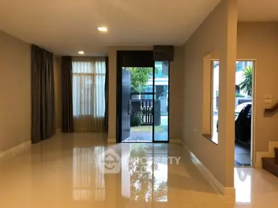 Spacious modern living room with large windows and glossy tiled floors, leading to a garden view.