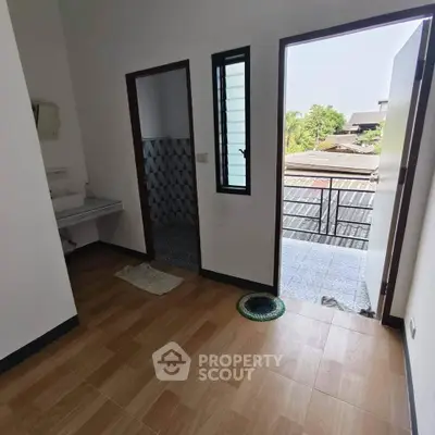 Cozy room with wooden flooring and balcony access, offering a serene view of the neighborhood.