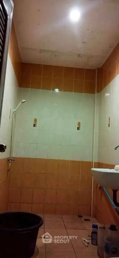 Compact bathroom with tiled walls and ceiling light, featuring a shower and sink.