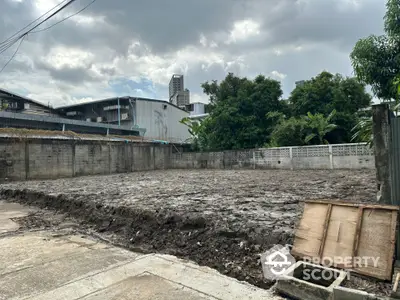 Vacant land plot in urban area with potential for development, surrounded by trees and buildings.