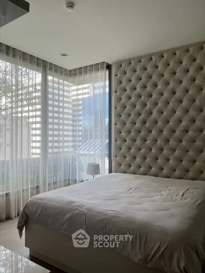 Luxurious bedroom with tufted wall and floor-to-ceiling windows offering city views.