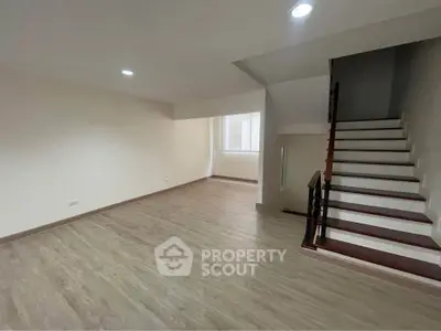 Spacious empty living room with wooden flooring and staircase, ideal for customization.