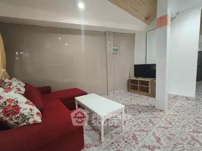 Cozy living room with red sofa and floral cushions, featuring a modern TV setup and tiled flooring.